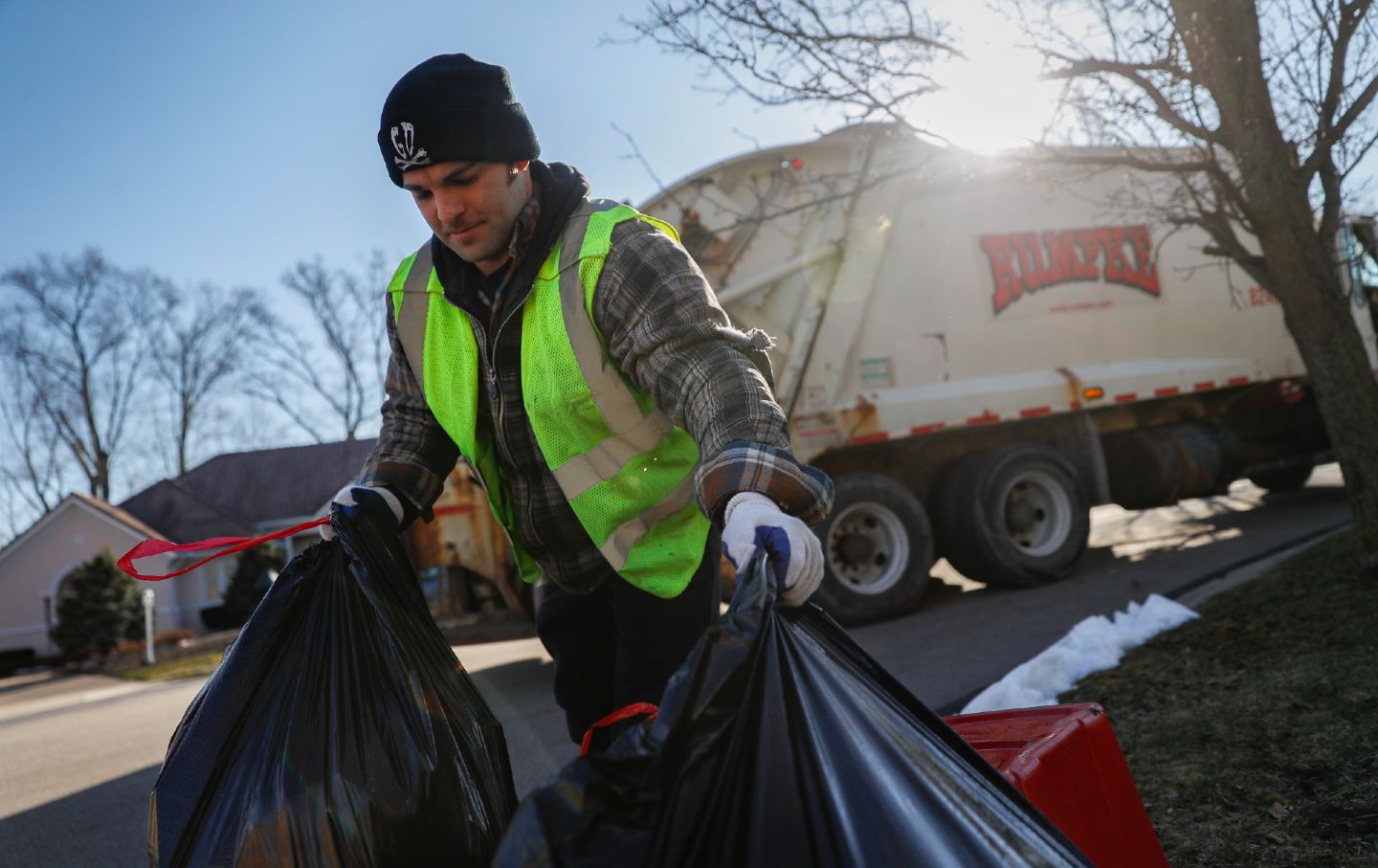 Sanitation Worker picking up trash bags in front of garbage truck